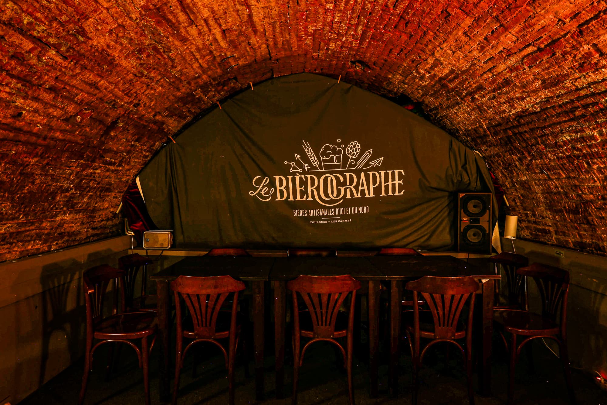 Le Bièrographe's brick-vaulted cellar with the branded backdrop and long communal table